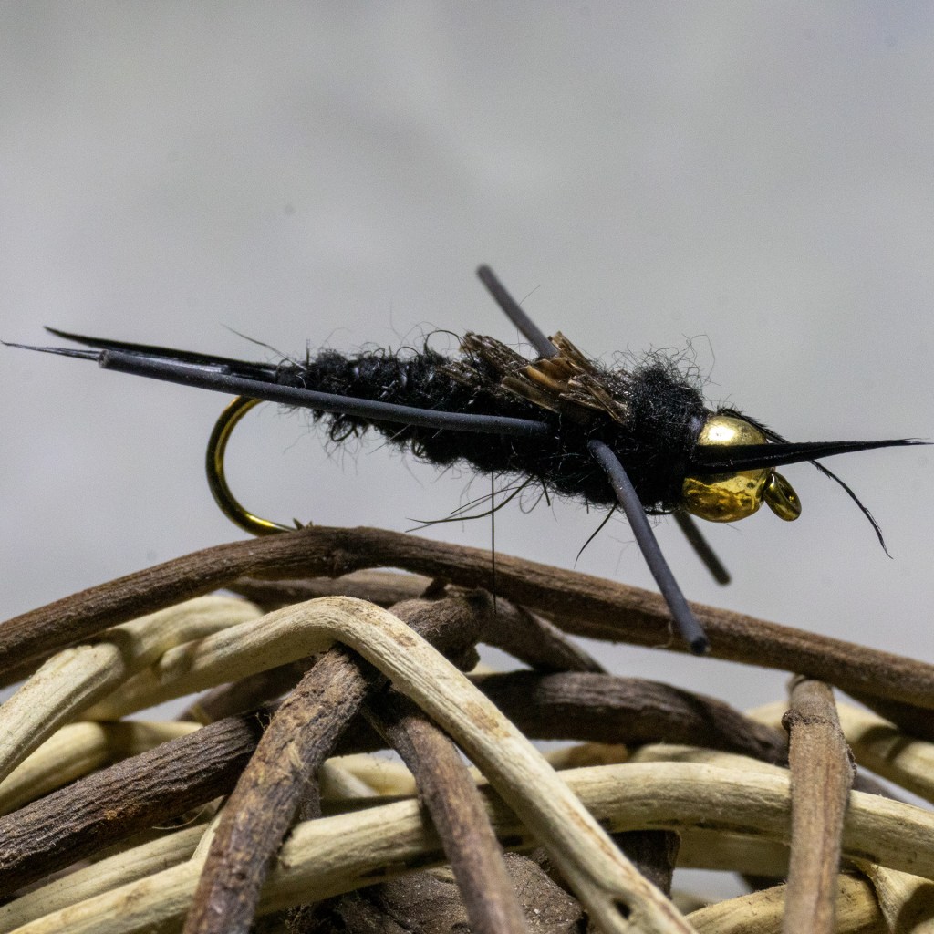 Close-up of a black fly with a gold bead head, resting on intertwined natural fibers.