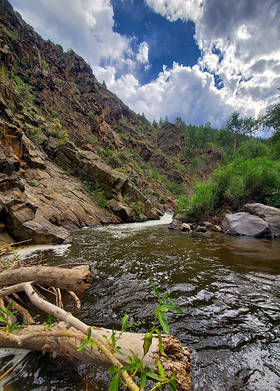 A scenic view of a winding creek surrounded by rocky cliffs and greenery under a partly cloudy sky.