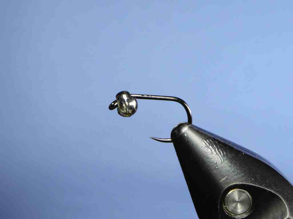 A close-up image of a fishing hook with a bead attached to it, against a blue background.