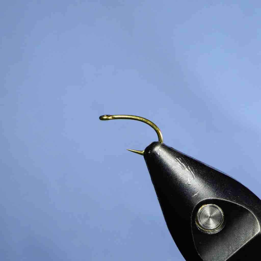 A close-up image of a hook placed in a vice, ready for tying a fly.